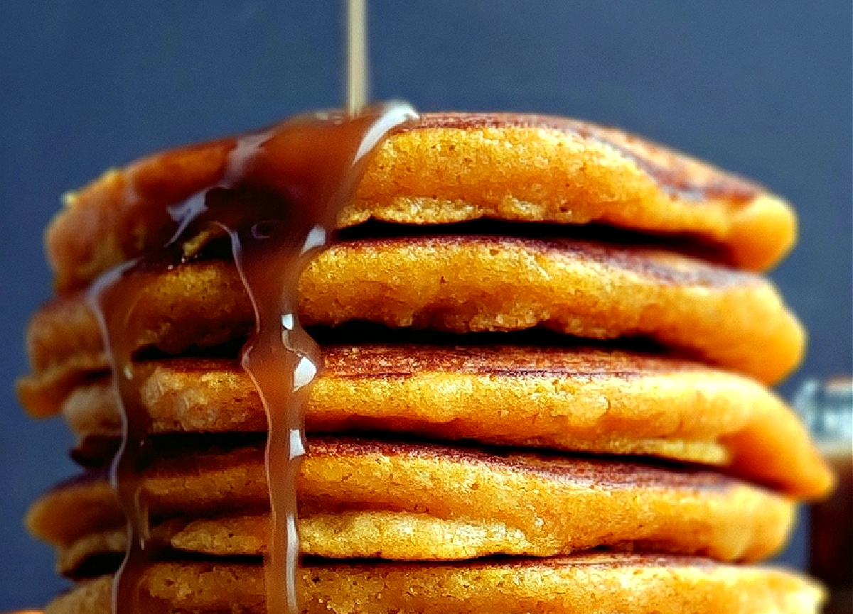 Pumpkin pancakes with cinnamon syrup pour. Cinnamon syrup being poured over a tall stack of pumpkin pancakes.