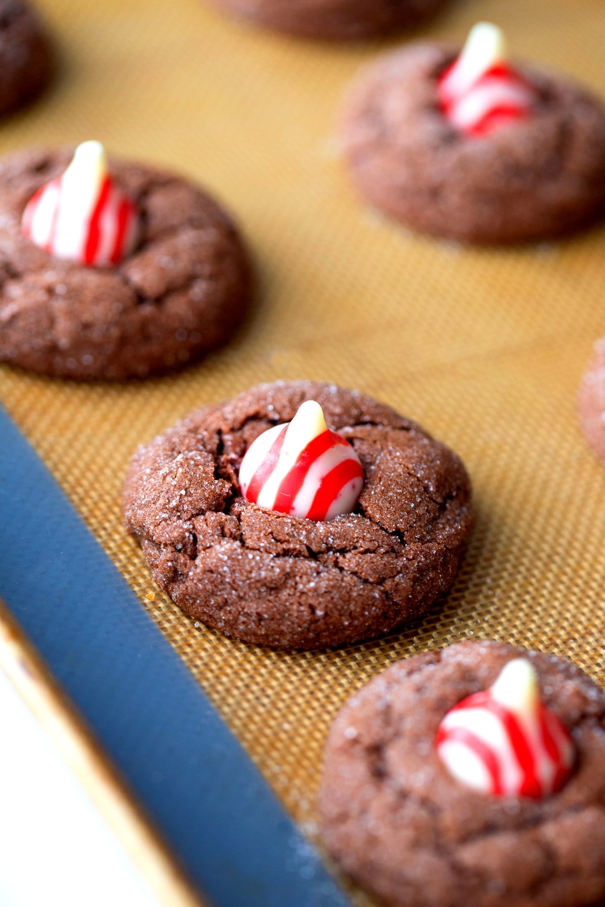 Cookies with Hershey's Kiss cooling on a silicone mat Baked Dark Chocolate Peppermint Crackle Cookies topped with a Hershey's Kiss, cooling on a silicone mat.