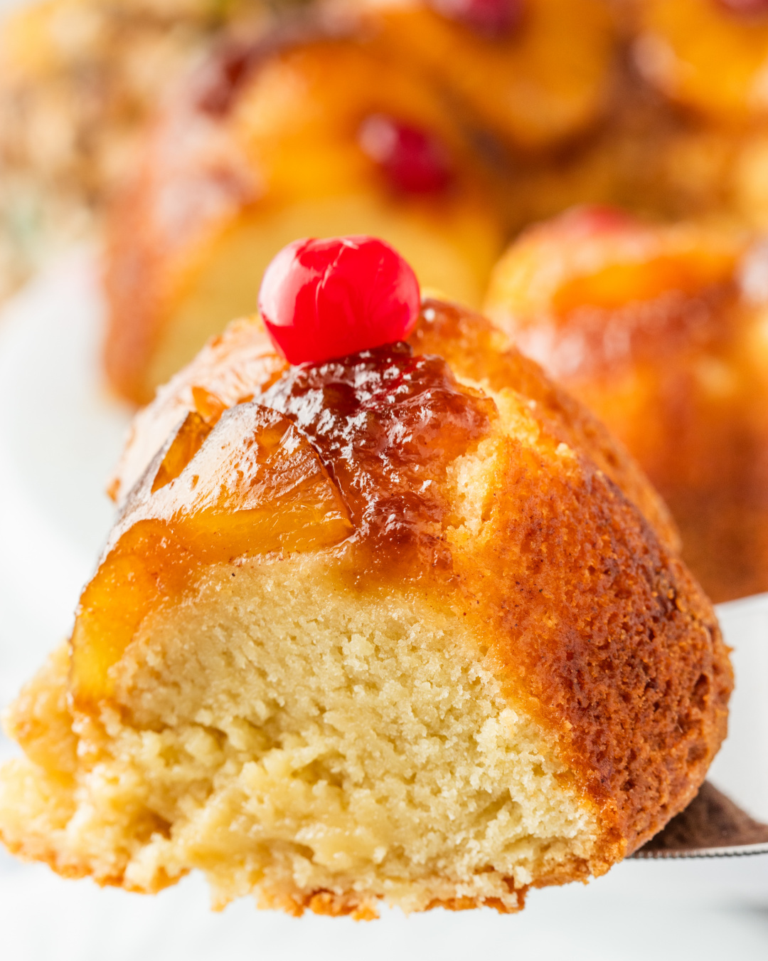 A single slice of pineapple upside down Bundt cake with golden edges and a cherry on top.