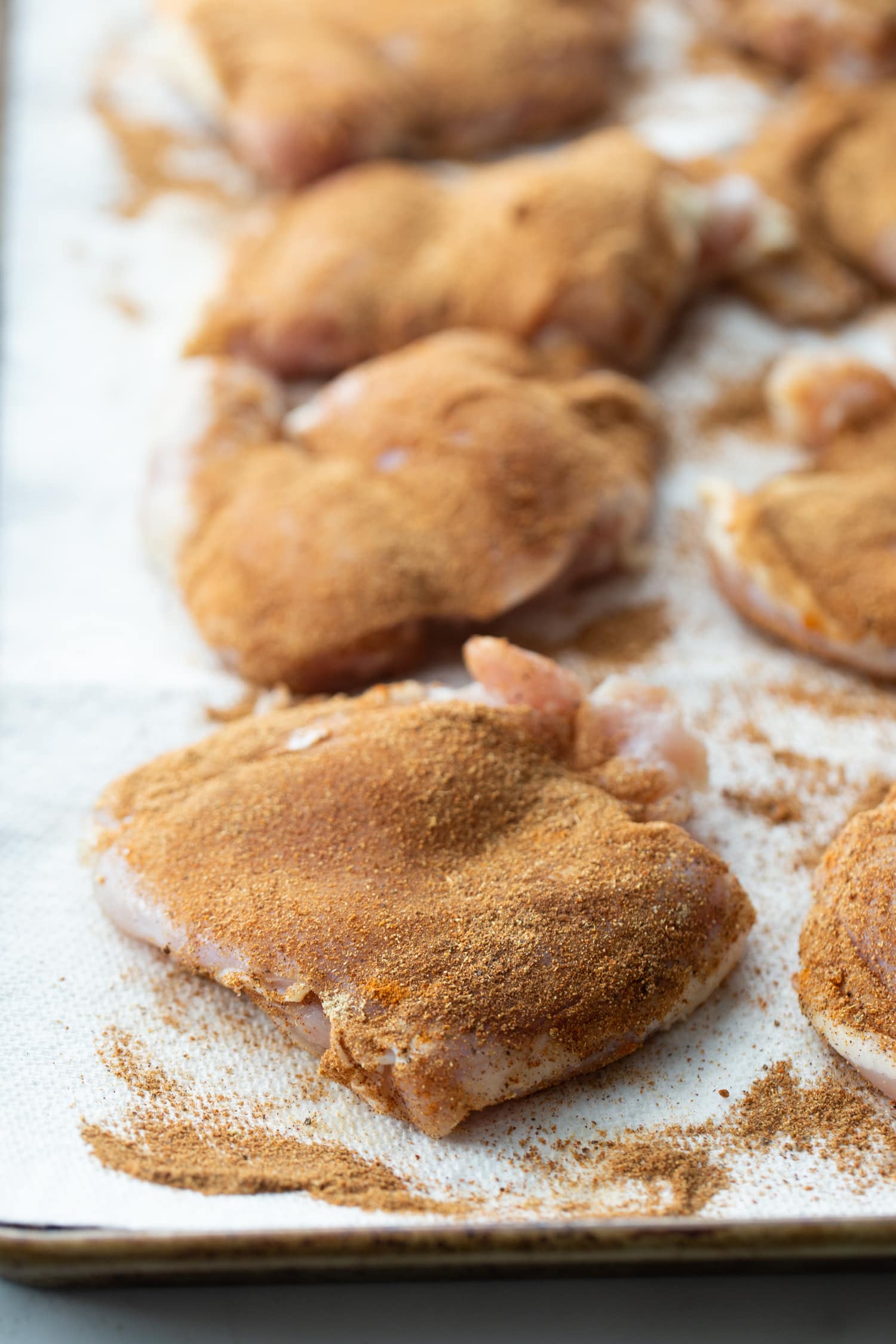 how to make Air Fryer Caribbean Spiced Chicken Raw chicken thighs on a baking sheet, evenly coated with the spice blend.