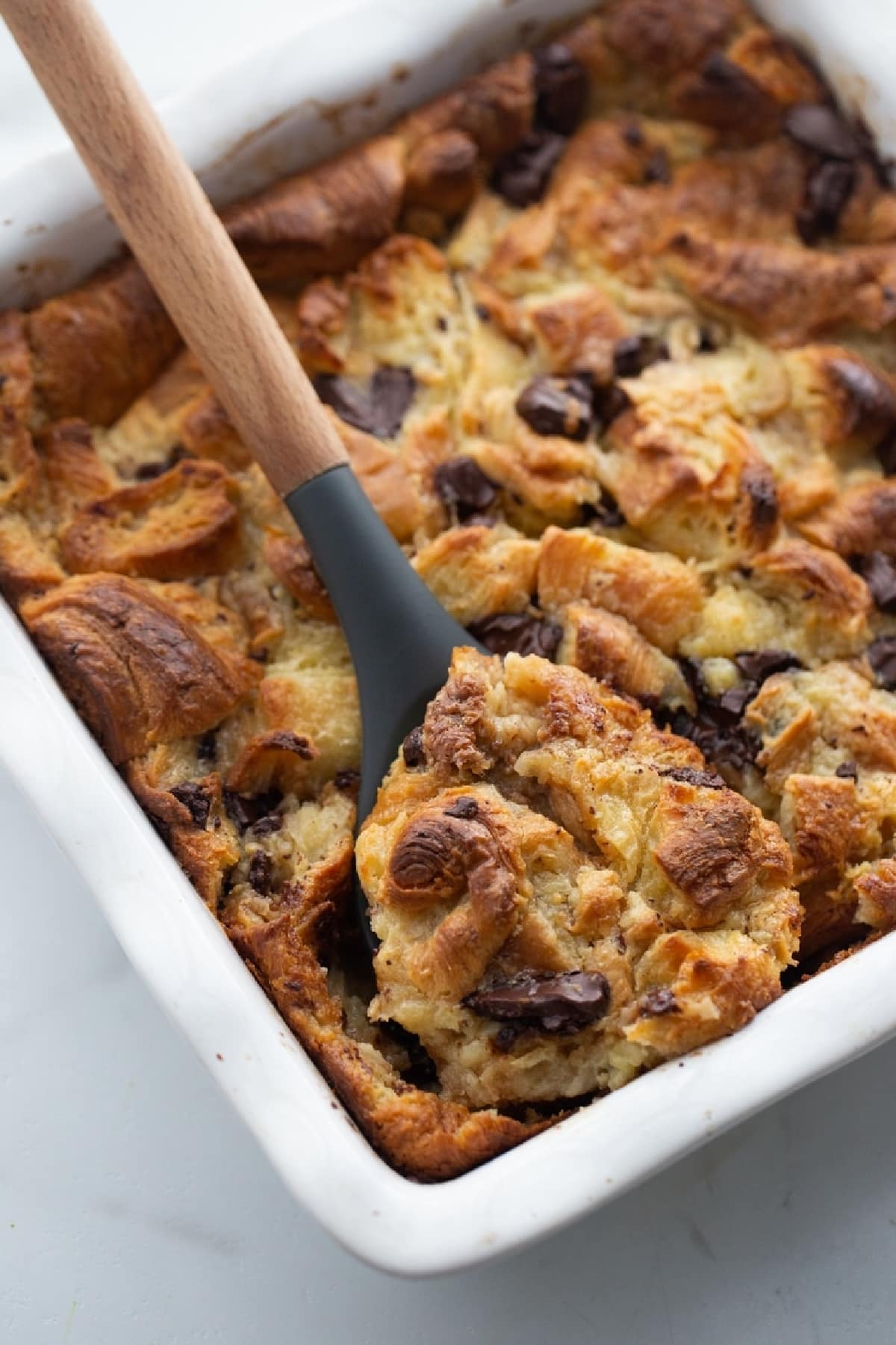 Chocolate Croissant Bread Pudding in a baking dish A spoon scooping out a portion of chocolate croissant bread pudding from a baking dish, showing the rich, custardy texture and melty chocolate.