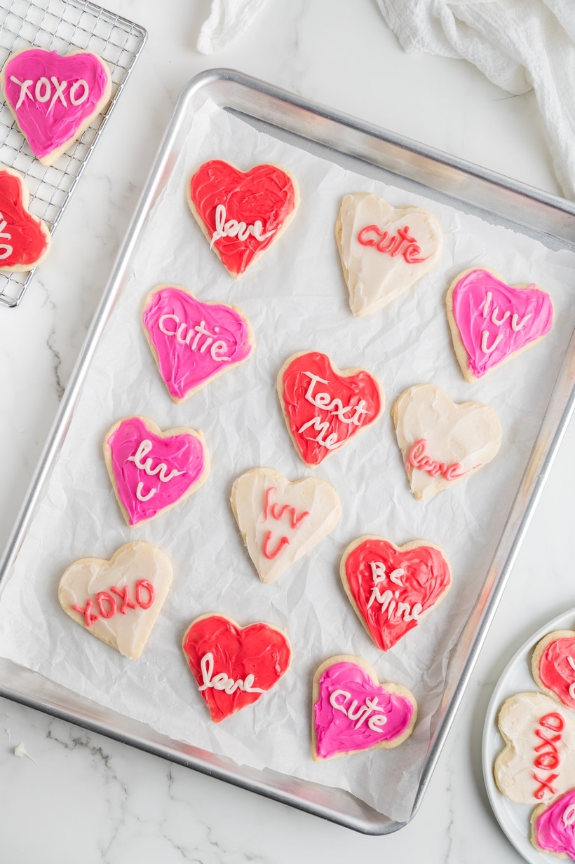 A baking sheet lined with freshly baked heart cookies before decorating, showing their smooth and even shape.
