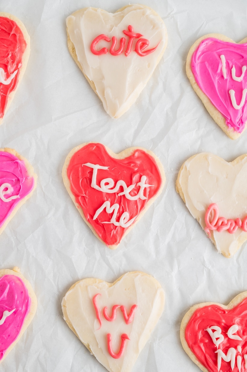 Close-up of heart-shaped sugar cookies decorated with pink, red, and white frosting, resembling conversation heart candies.