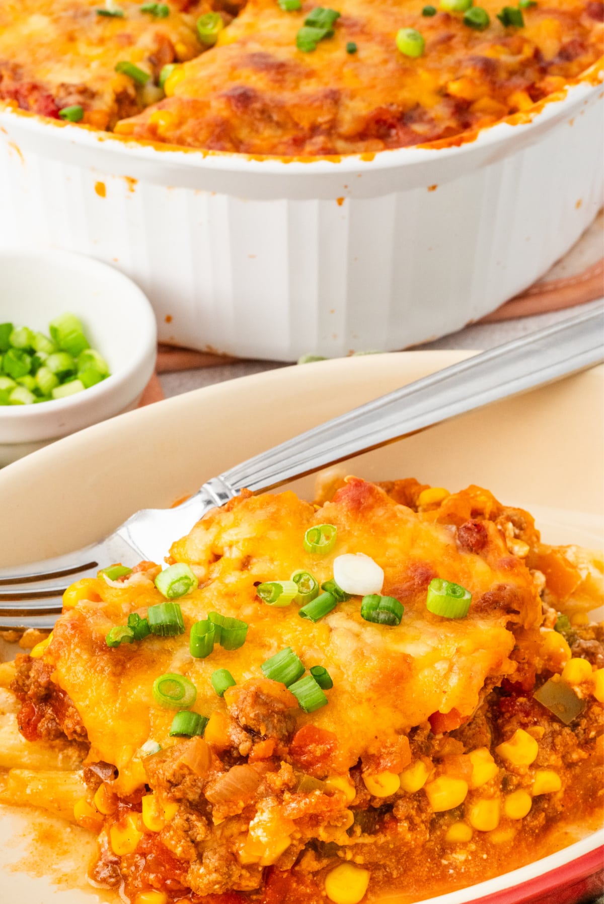 Serving of cheesy ground beef casserole with peppers, corn, and pasta Slice of easy ground beef casserole with pasta, corn, and melted cheddar cheese on a plate