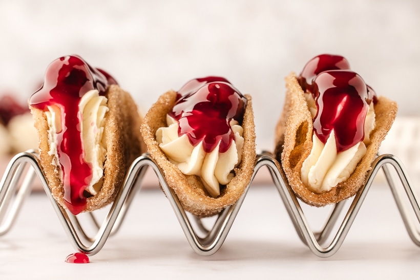Three Mini Cherry Cheesecake Tacos in a Holder Three mini cherry cheesecake tacos in a taco holder, showcasing the crispy cinnamon-sugar shells and creamy cheesecake filling.