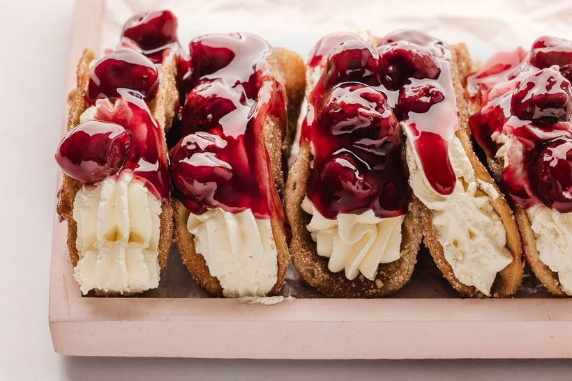 Cherry Cheesecake Tacos Standing Upright and Stuffed Full view of multiple cherry cheesecake tacos standing upright, filled with cheesecake and topped with cherry pie filling.
