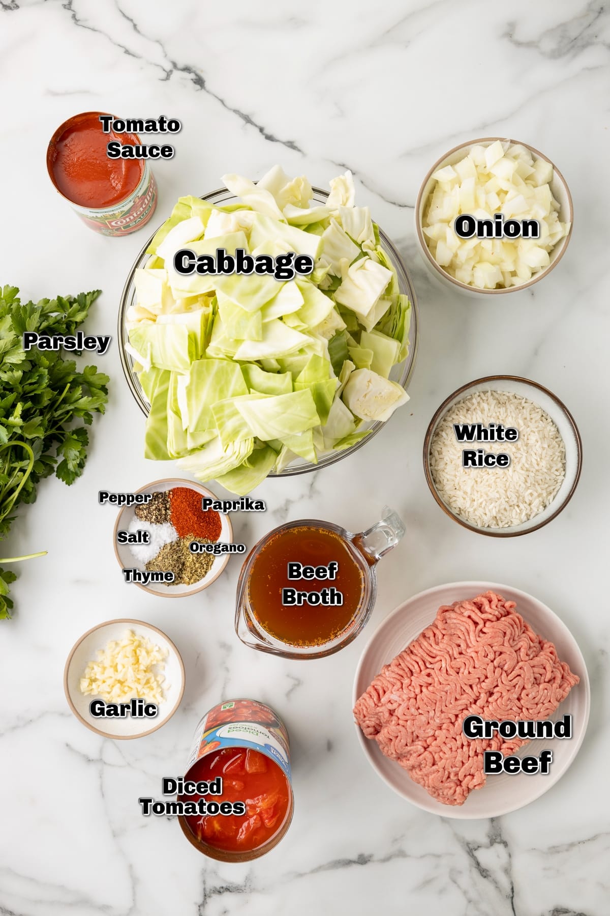 Ingredients for unstuffed cabbage rolls including cabbage, beef, rice, tomatoes, broth, and spices on a marble counter.