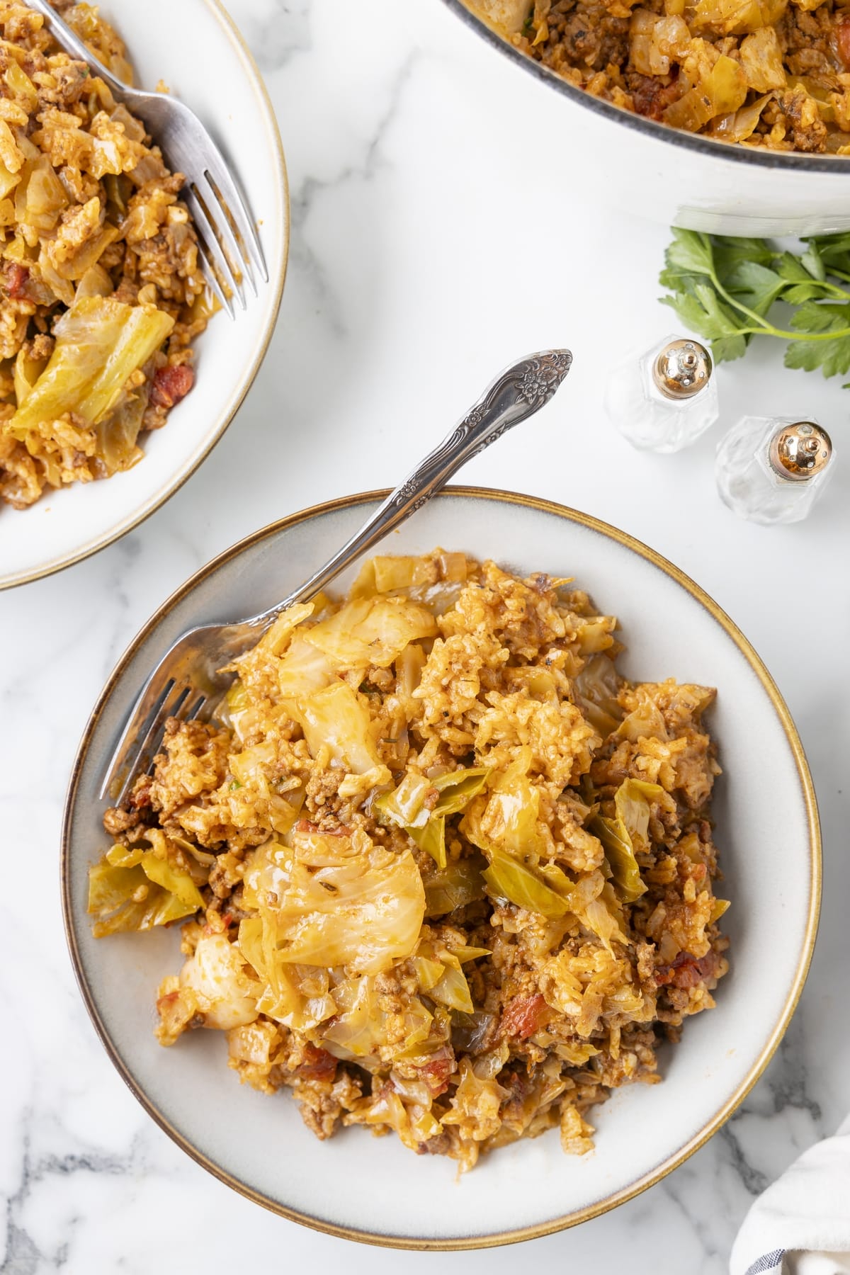 Overhead view of unstuffed cabbage rolls with beef, rice, and cabbage served in bowls with forks.