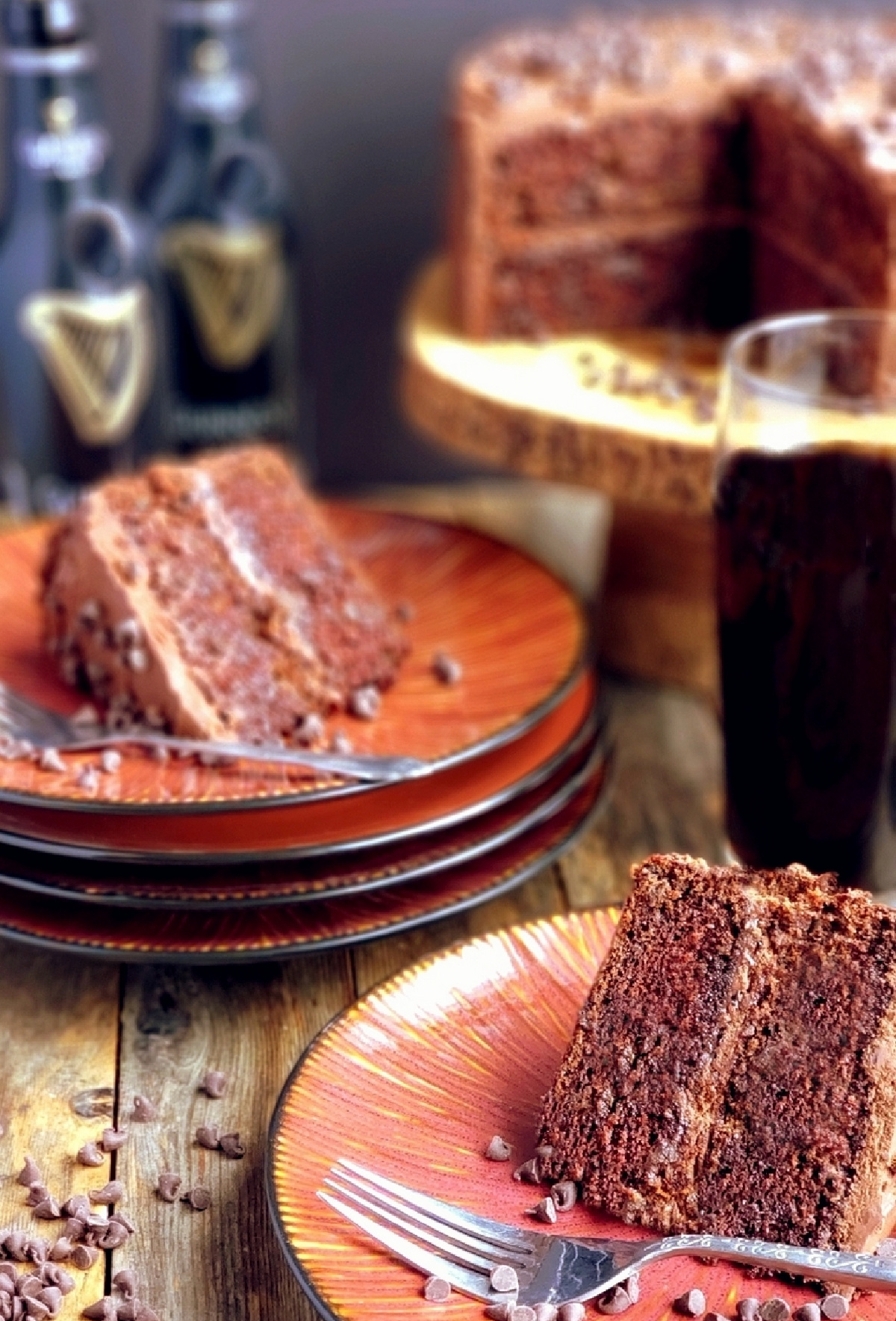 slice of Guinness chocolate layer cake on orange plate with stout and whole cake in background