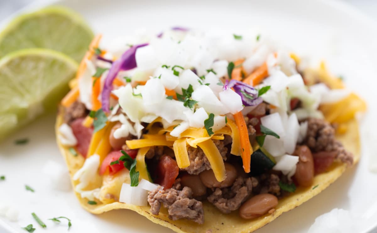 Side angle of stacked tostada showing beef, cheese, and lime slaw layers