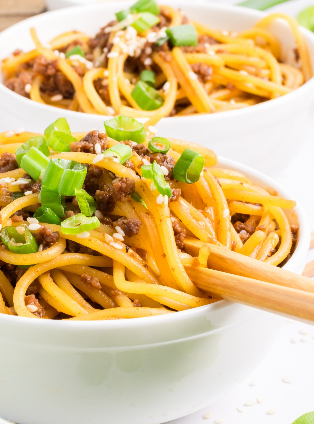 Mongolian beef noodles with green onions Bowl of Mongolian beef noodles topped with green onions and sesame seeds, sauce-coated noodles twirled with chopsticks by Noble Pig.