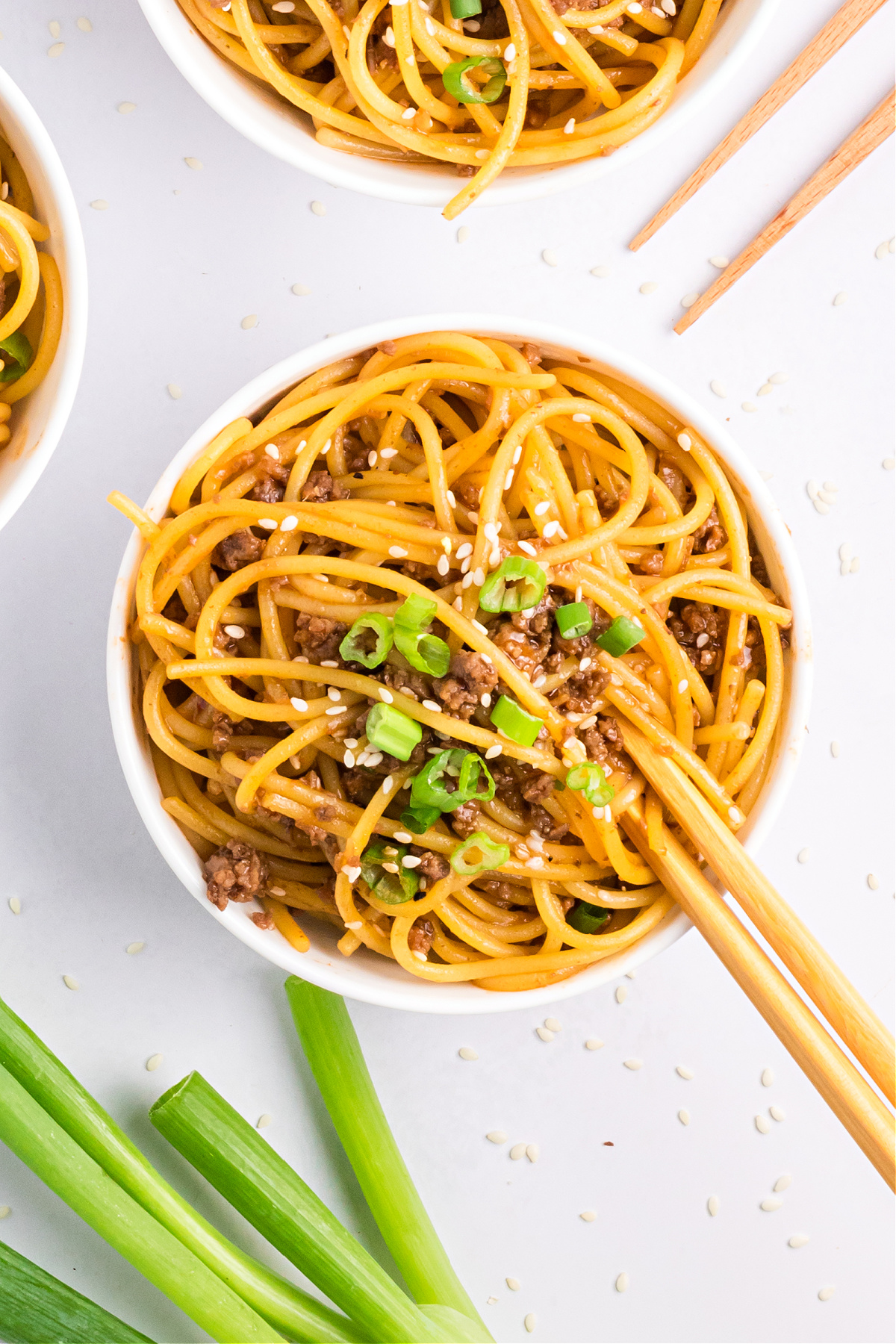 Easy Mongolian beef noodles recipe Easy Mongolian beef noodles recipe in a bowl with chopsticks, topped with sesame seeds and sliced green onions.