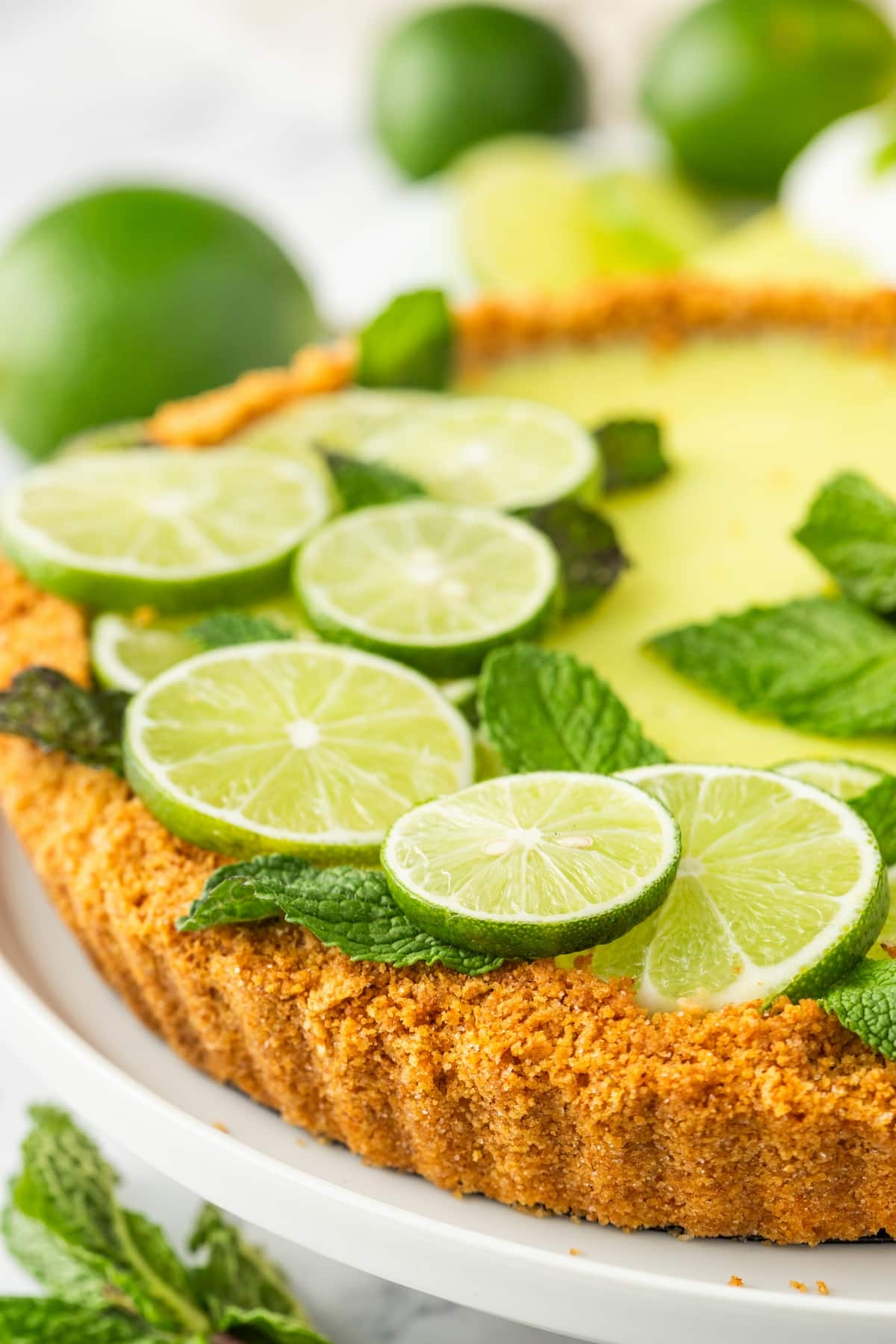 Close-up of Key lime tart with lime slices and mint, showing crisp graham cracker crust