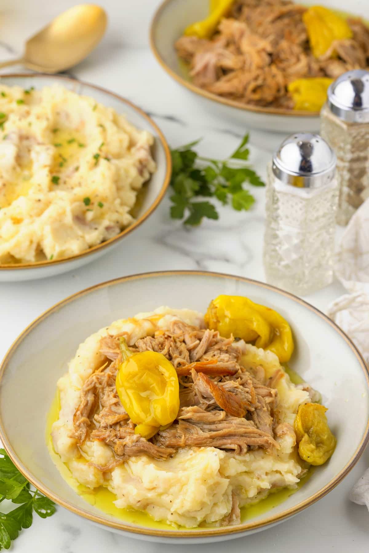 Slow Cooker Pork Roast Dinner with Mashed Potatoes Slow cooker Mississippi pork roast on mashed potatoes with pepperoncini peppers, with additional mashed potatoes and pork in the background.