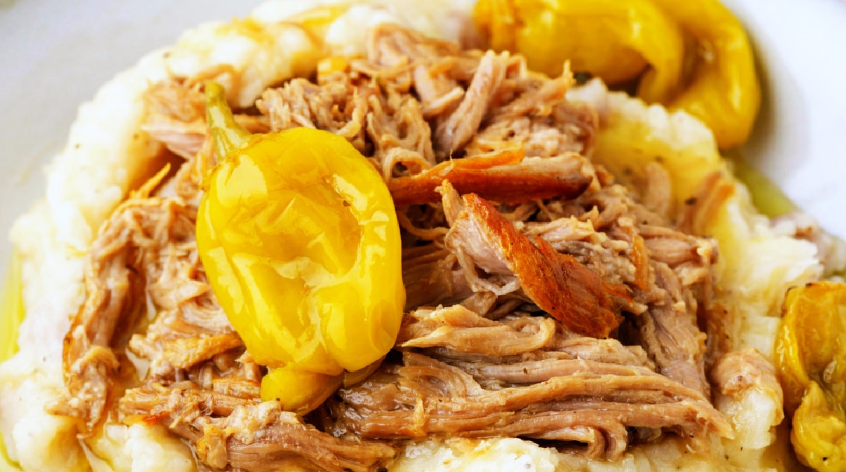Mississippi Pork Close-up of shredded Mississippi pork roast with browned strands of pork, whole pepperoncini peppers, and mashed potatoes.