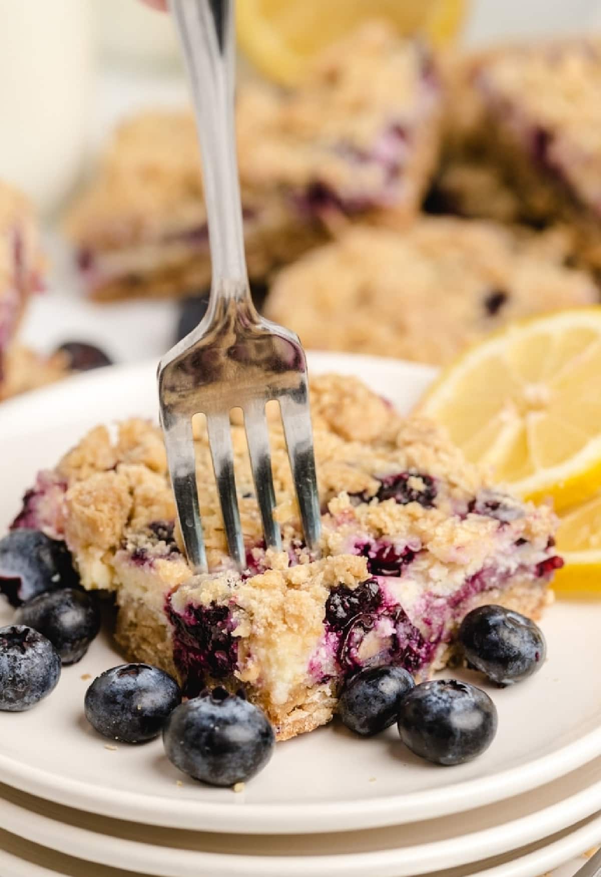 Close-up of a fork taking a bite of lemon blueberry bar Fork cutting into a lemon blueberry crumble bar on a white plate