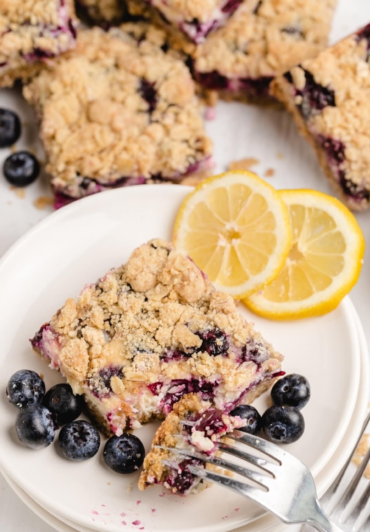 Creamy lemon blueberry bar with bite taken out Fork pulling a bite from a sliced lemon blueberry crumble bar