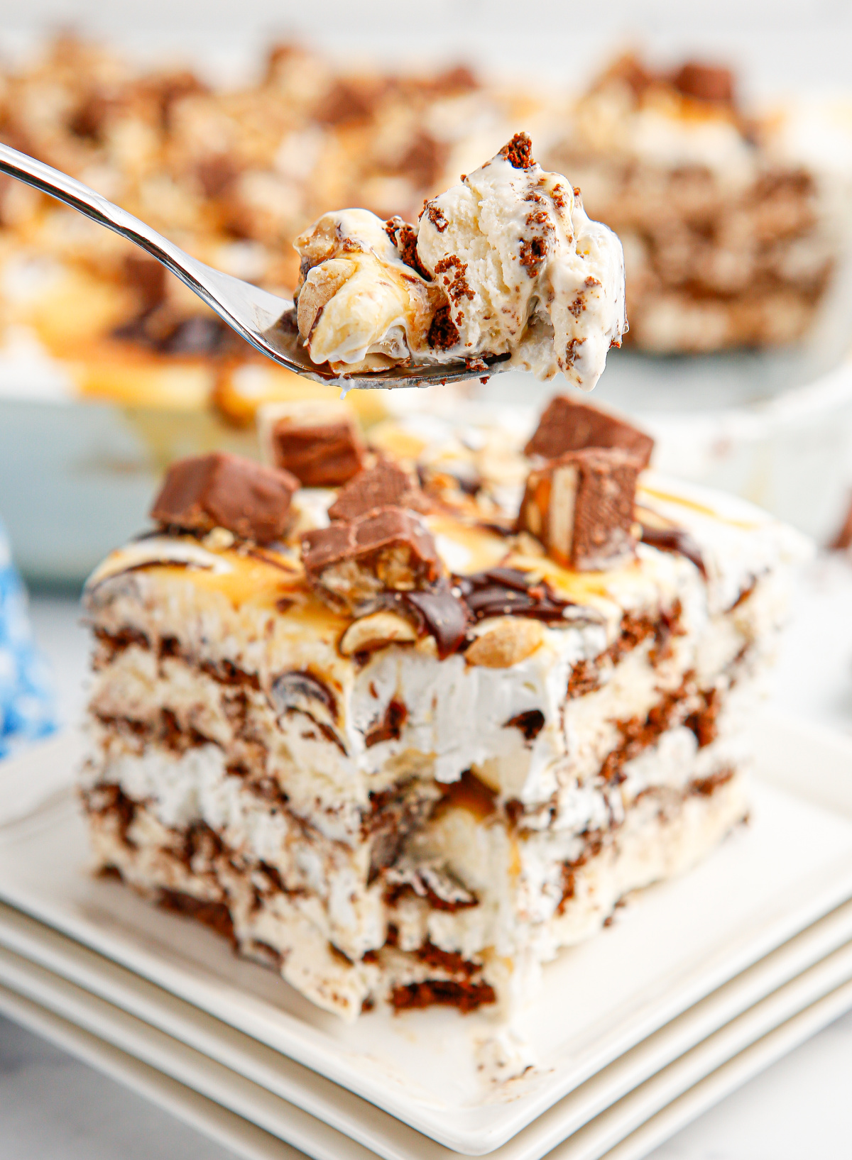 Spoonful of frozen snickers ice cream sandwich cake showing layers of whipped topping and crushed candy