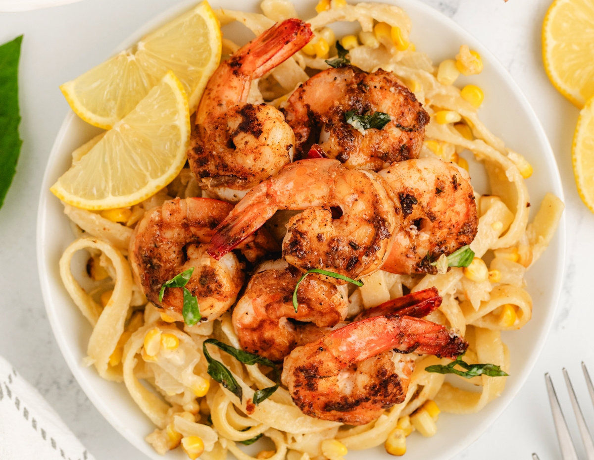 Bowl of blackened shrimp fettuccine with corn and lemon slices.