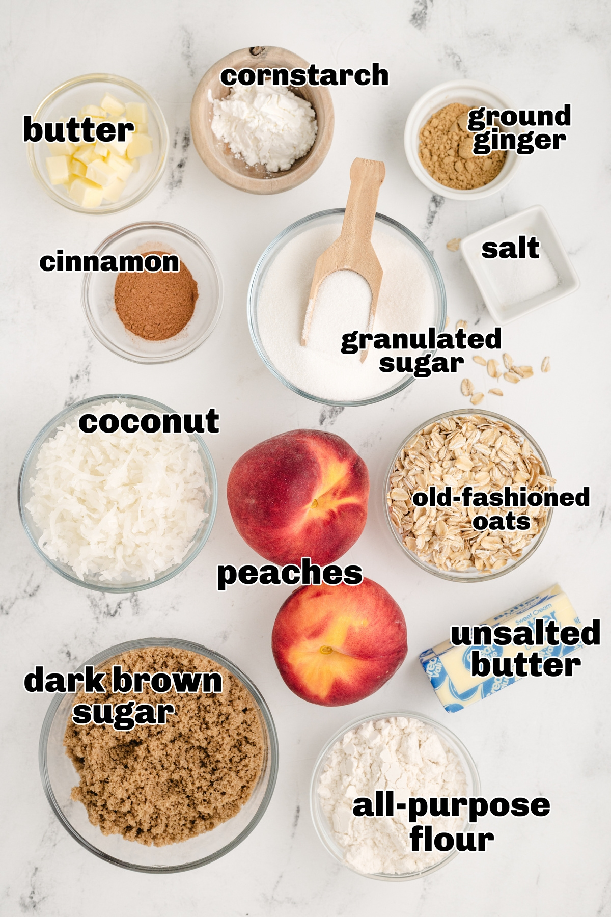 Coconut peach crisp ingredients laid out on counter. Overhead view of labeled ingredients for coconut peach crisp, including fresh peaches, oats, and shredded coconut.