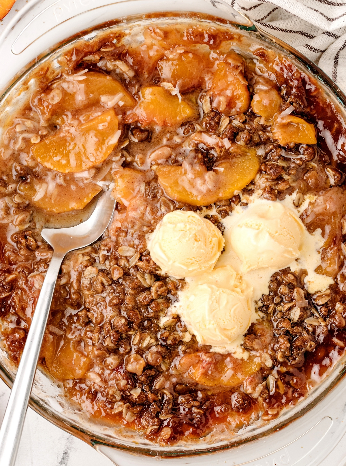 Baked peach crisp with ice cream. Freshly baked peach crisp in a pie dish with scoops of ice cream melting on top.