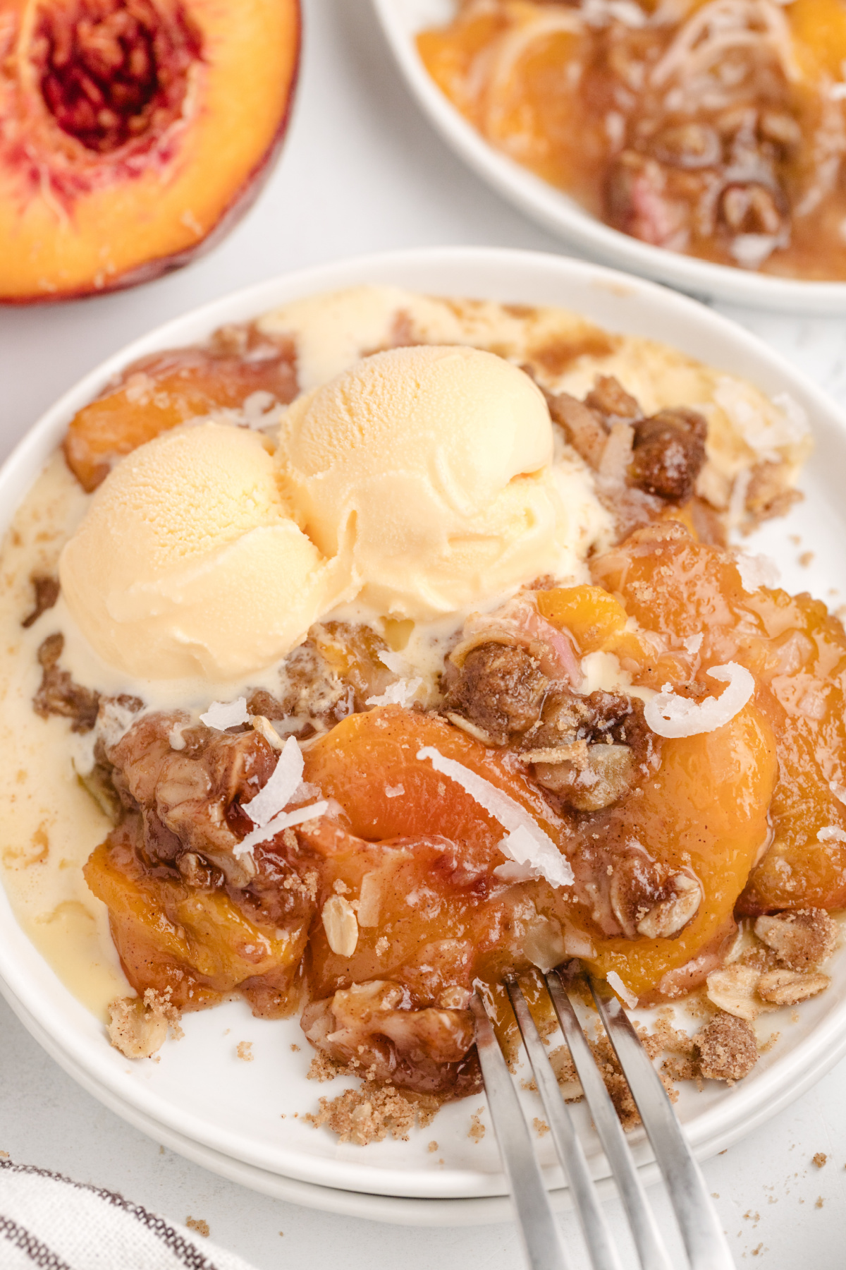 Coconut peach crisp served with vanilla ice cream. Close-up of a serving of coconut peach crisp with melting ice cream on a white plate.