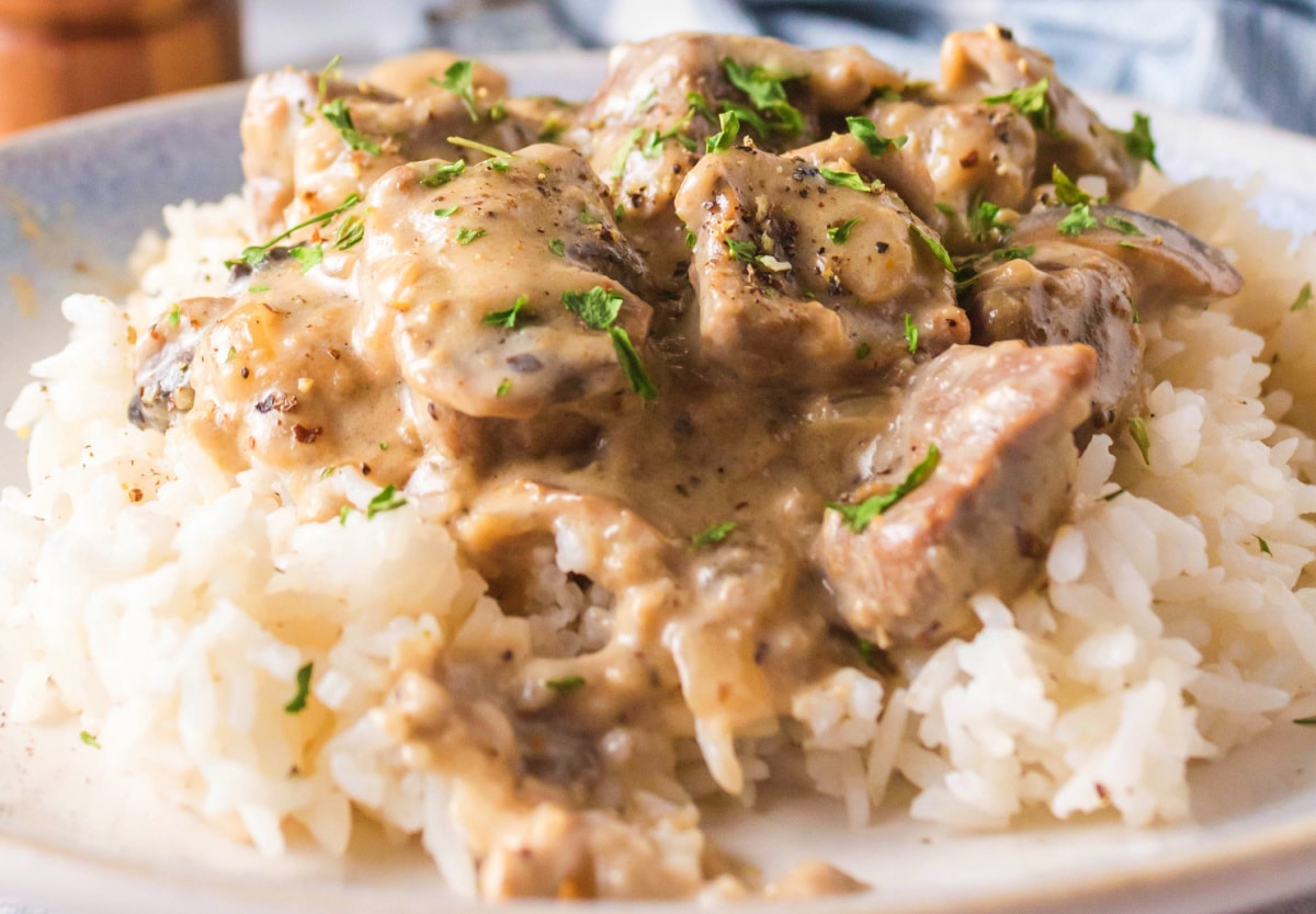 Overhead view of beef stroganoff on a white plate with rice and parsley garnish 