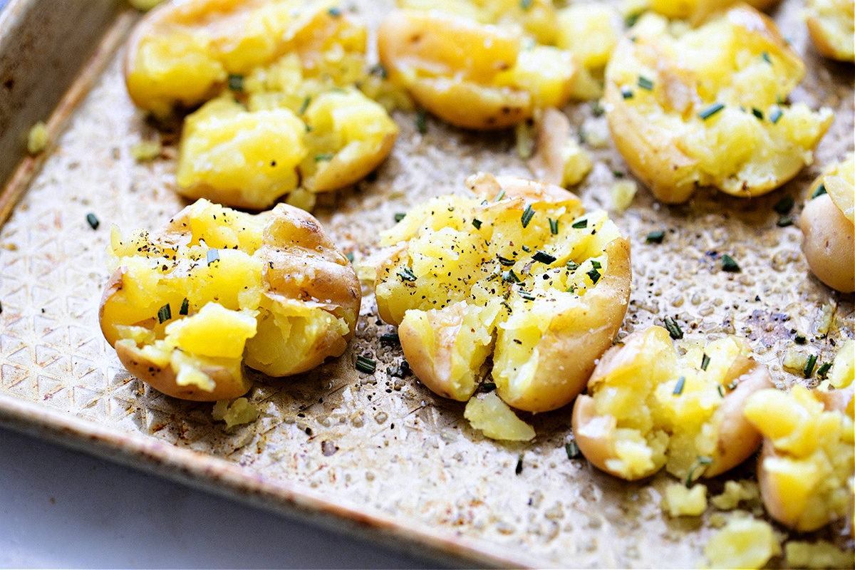 sheet pan potatoes, smashed potatoes, rosemary potatoes, Noble Pig Salt and vinegar smashed potatoes on a sheet pan, crisped and seasoned with rosemary and pepper, showing their hand-smashed texture, by Noble Pig.
