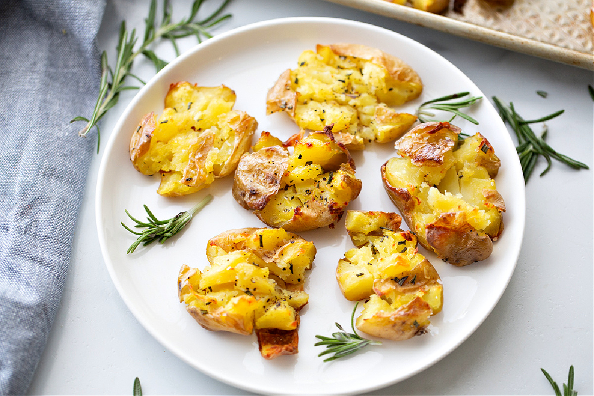 smashed potatoes, rosemary potatoes, roasted potatoes, crisp potatoes Crispy smashed potatoes on a white plate with rosemary, showing their golden edges and fluffy centers after roasting.
