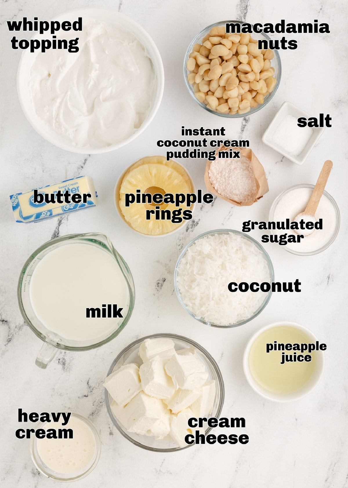 Ingredients for Hawaiian Dream Dessert Cups with macadamia nuts and coconut pudding Ingredients for Hawaiian Dream Dessert Cups including macadamia nuts, coconut cream pudding mix, pineapple rings, coconut, and cream cheese arranged on a marble surface.
