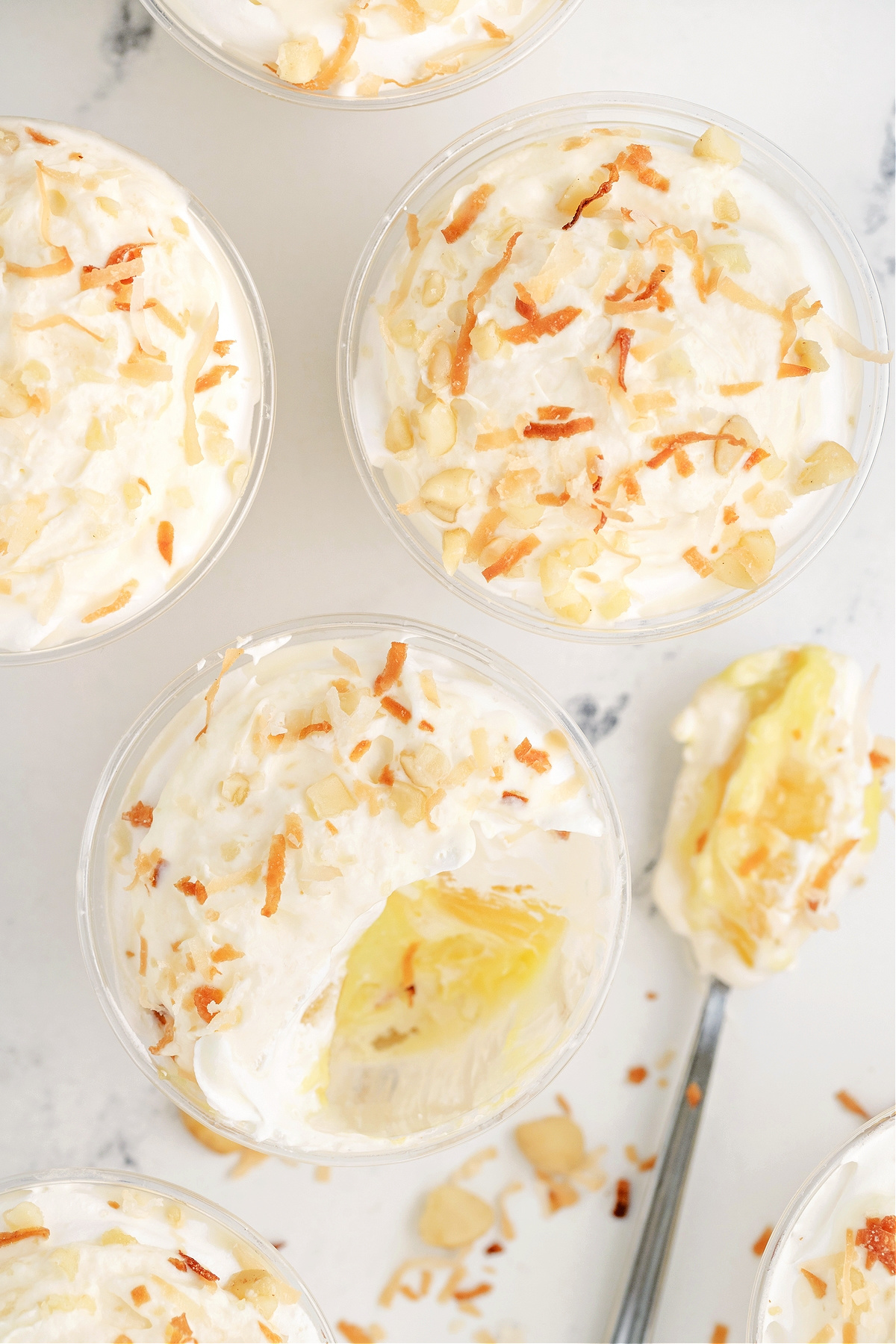 Hawaiian Dream Dessert Cups showing creamy pineapple and coconut layers Overhead view of Hawaiian Dream Dessert Cups with one cup showing a spoonful removed to reveal creamy layers of pineapple and coconut.
