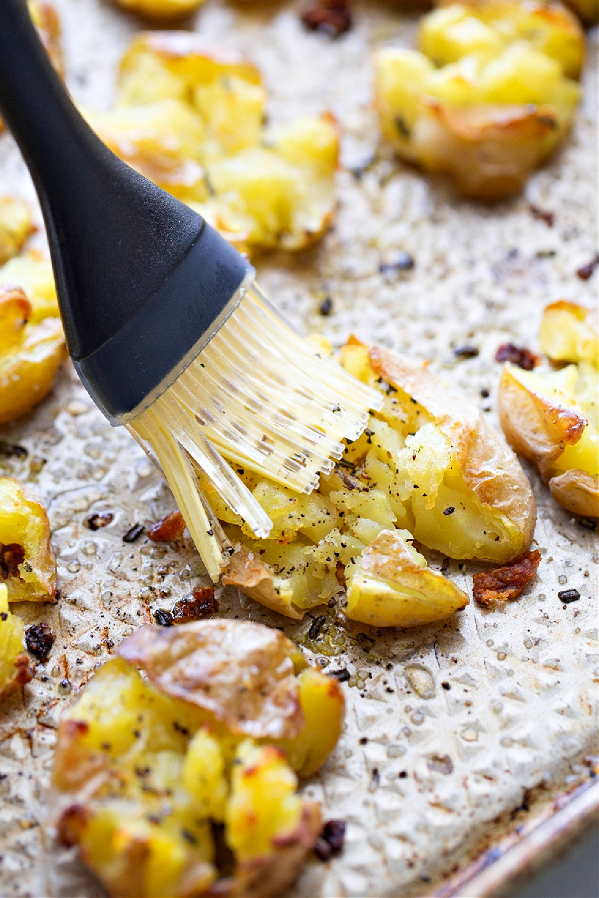 brushing vinegar on potatoes, vinegar step potatoes, sheet pan potatoes, finishing potatoes A pastry brush adding apple cider vinegar to hot smashed potatoes on a sheet pan, giving salt and vinegar smashed potatoes their tang.