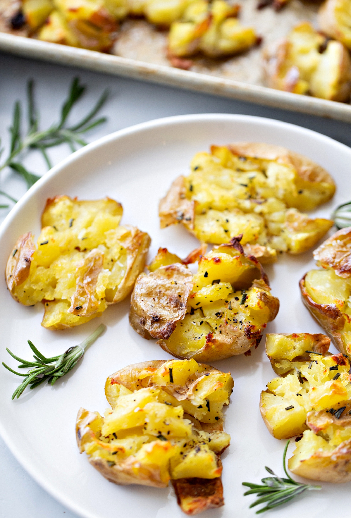salt and vinegar smashed potatoes, roasted potatoes, rosemary potatoes, Noble Pig Salt and vinegar smashed potatoes with crisp edges and rosemary on a white plate, showing their roasted texture, by Noble Pig.
