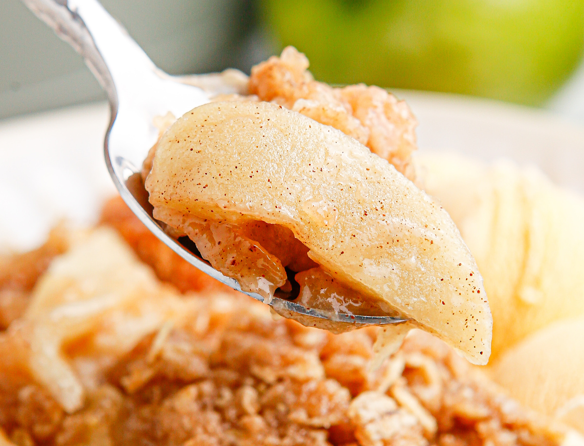 A spoonful of tender cinnamon apples from a crockpot apple crisp showing the soft filling texture.