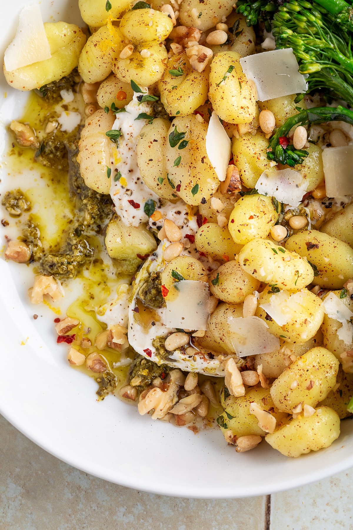Finished gnocchi with burrata, pesto, and brown butter sauce. Overhead shot of gnocchi with burrata, basil pesto, toasted nuts, and parmesan shavings.