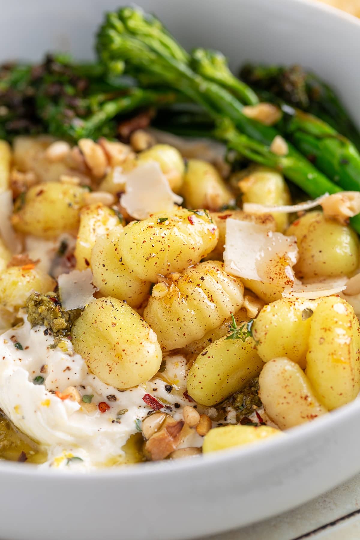 Brown butter gnocchi with burrata, pesto, and broccolini. Side view of gnocchi with burrata and pesto, served with broccolini and topped with parmesan shavings.