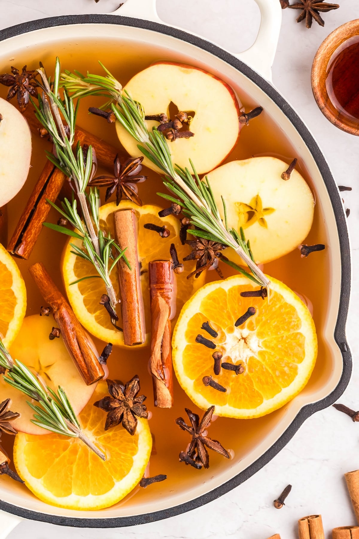 Overhead view of a simmering pot with seasonal ingredients in a white cast iron skillet.