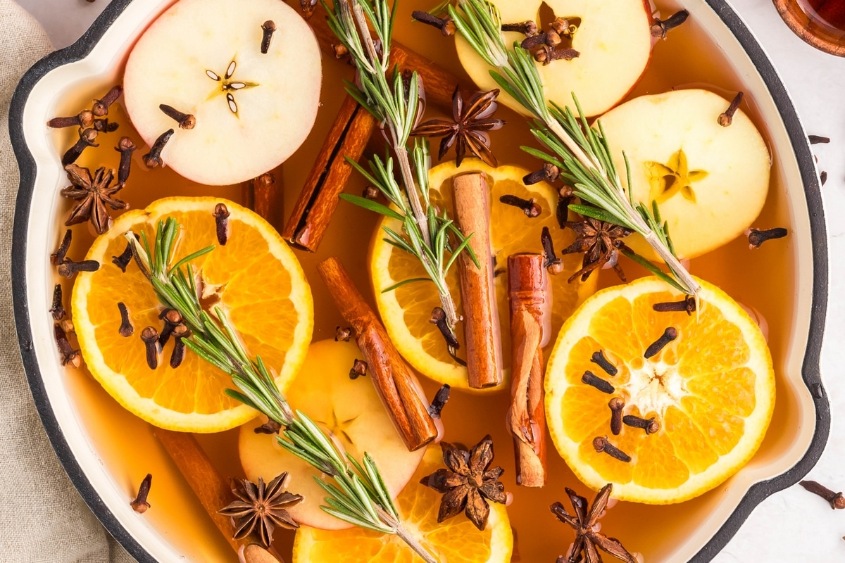 Overhead of a simmer pot with oranges, cinnamon, and cloves in a white skillet.