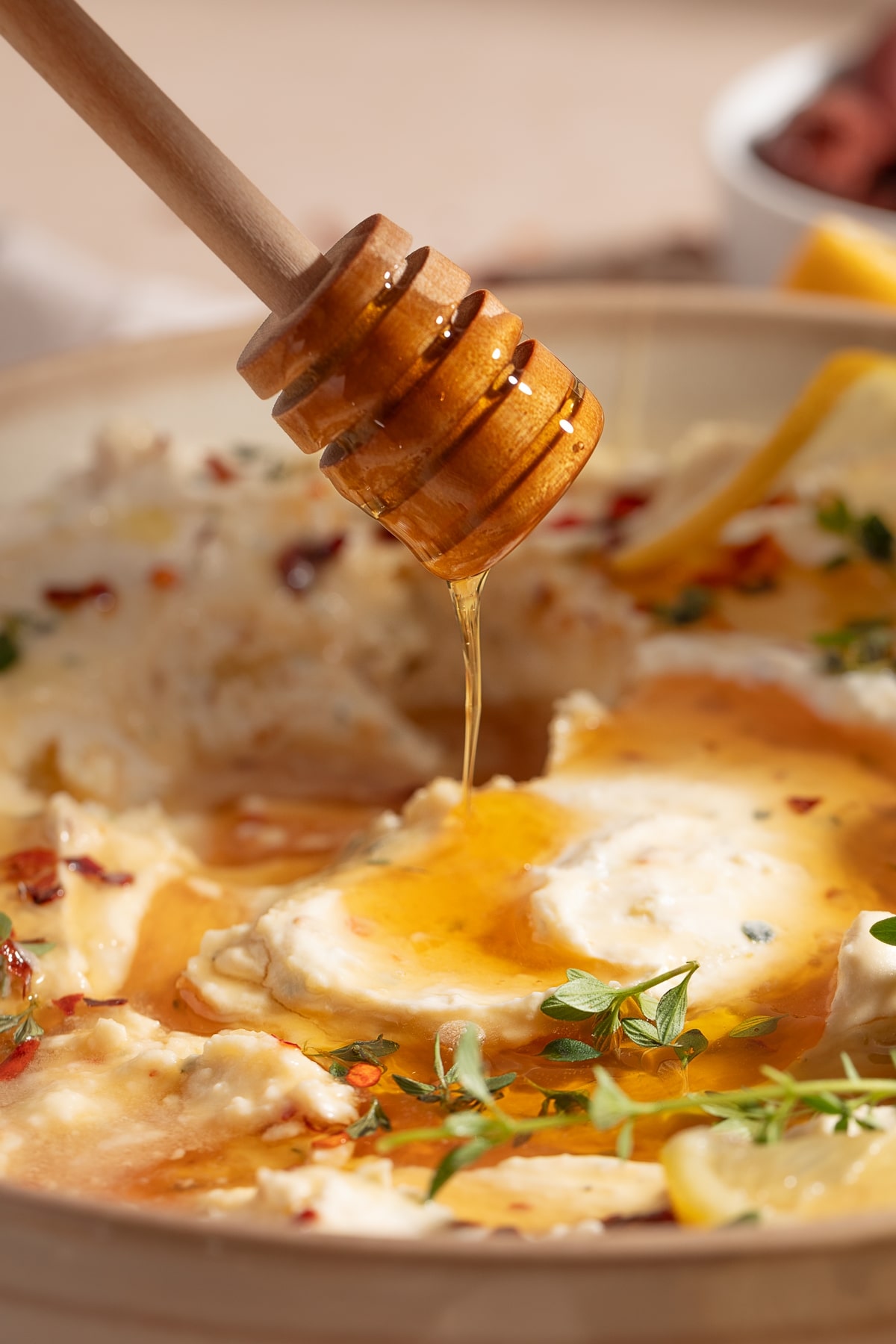 Side View of Whipped Feta Dip with Honey Drizzling Side view of whipped feta roasted garlic dip with honey, showing a honey wand dropping honey into the dip.