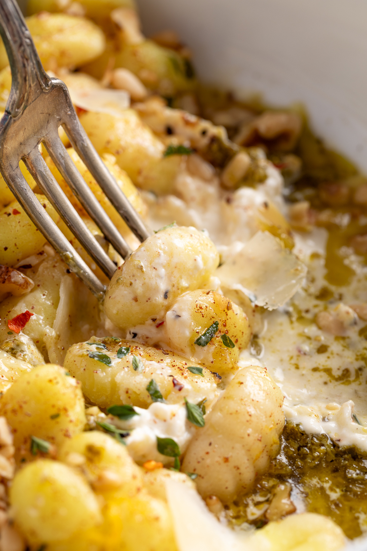 Fork lifting gnocchi with burrata and pesto. Fork twirling gnocchi over melted burrata with pesto and fresh herbs.
