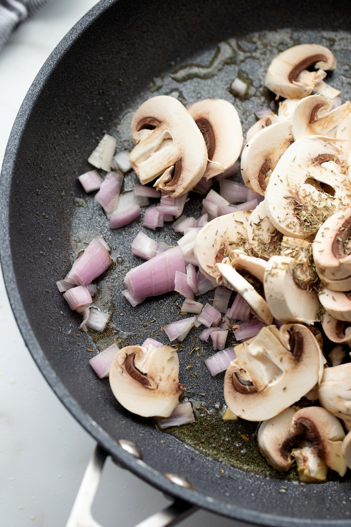 Mushrooms, shallots, and thyme cooking in a skillet for pork Marsala.
