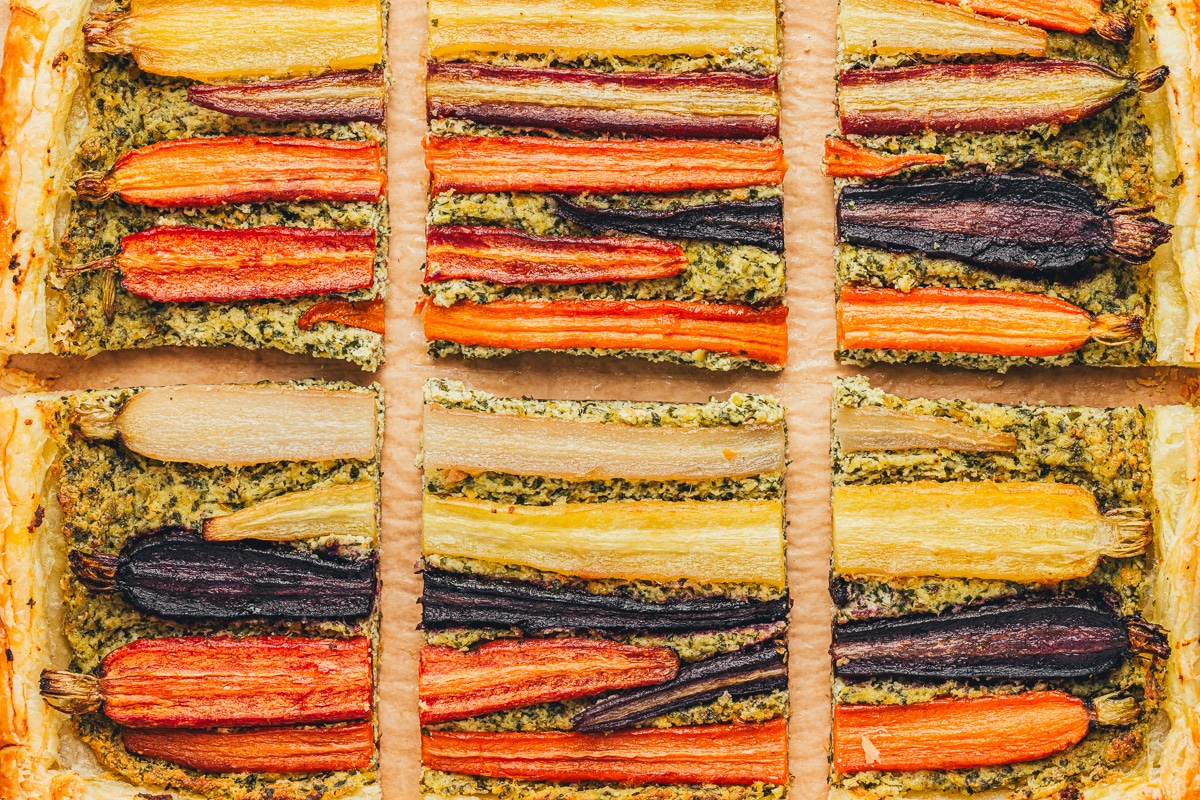 A detailed view of the tart’s toppings, showing the roasted rainbow carrots, green pesto, and golden edges of the pastry.