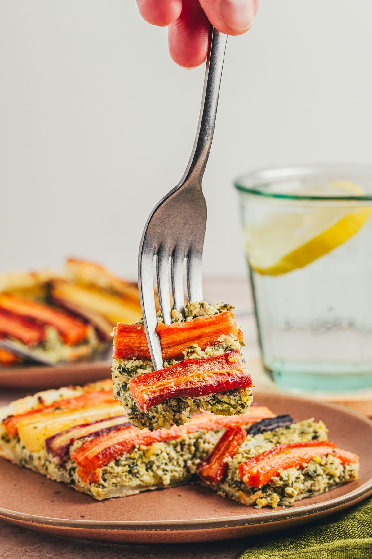A fork lifting a bite-sized piece of carrot tart, showing the flaky pastry, creamy pesto-ricotta layer, and tender roasted carrots.