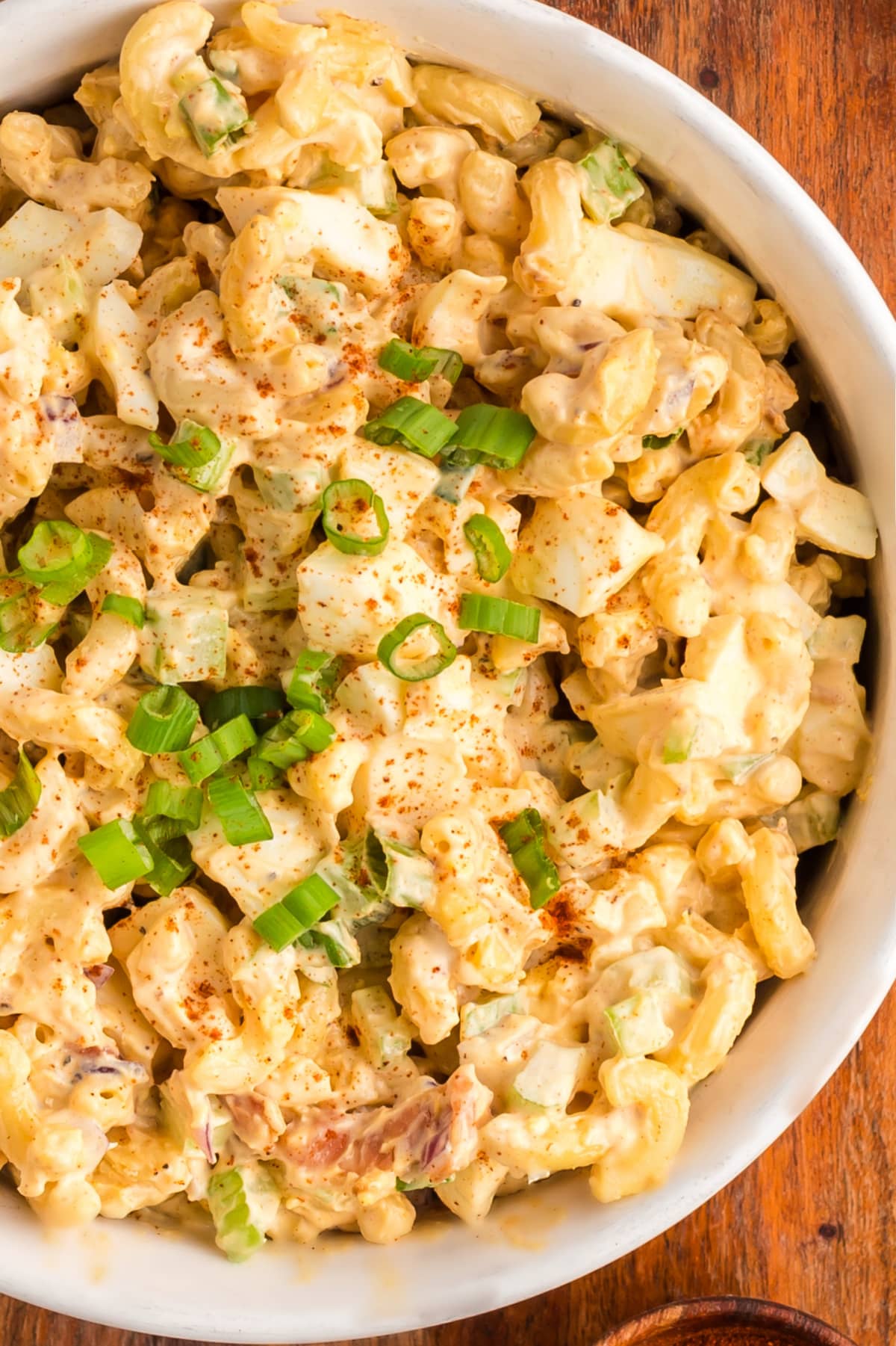 A top-down view of deviled egg pasta salad in a large bowl, showing creamy pasta, bacon, and green onions.