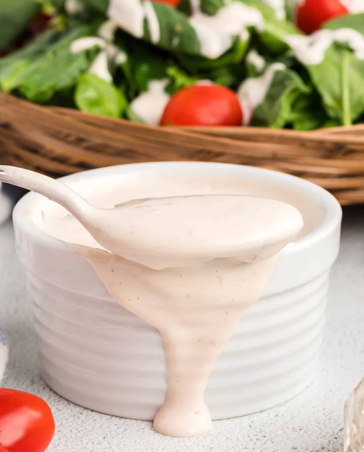 Spoon lifting out creamy salad dressing with some spilling over the side of the ramekin