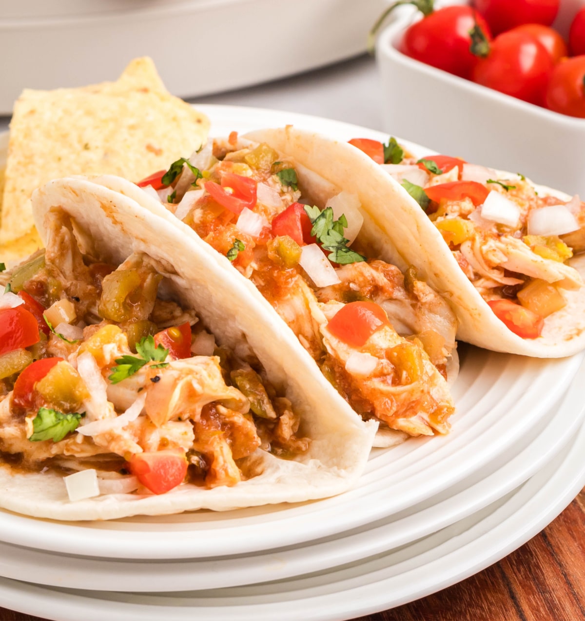 Three Slow Cooker Shredded Taco Chicken Three tacos filled with shredded chicken, salsa, and toppings, shown close-up.