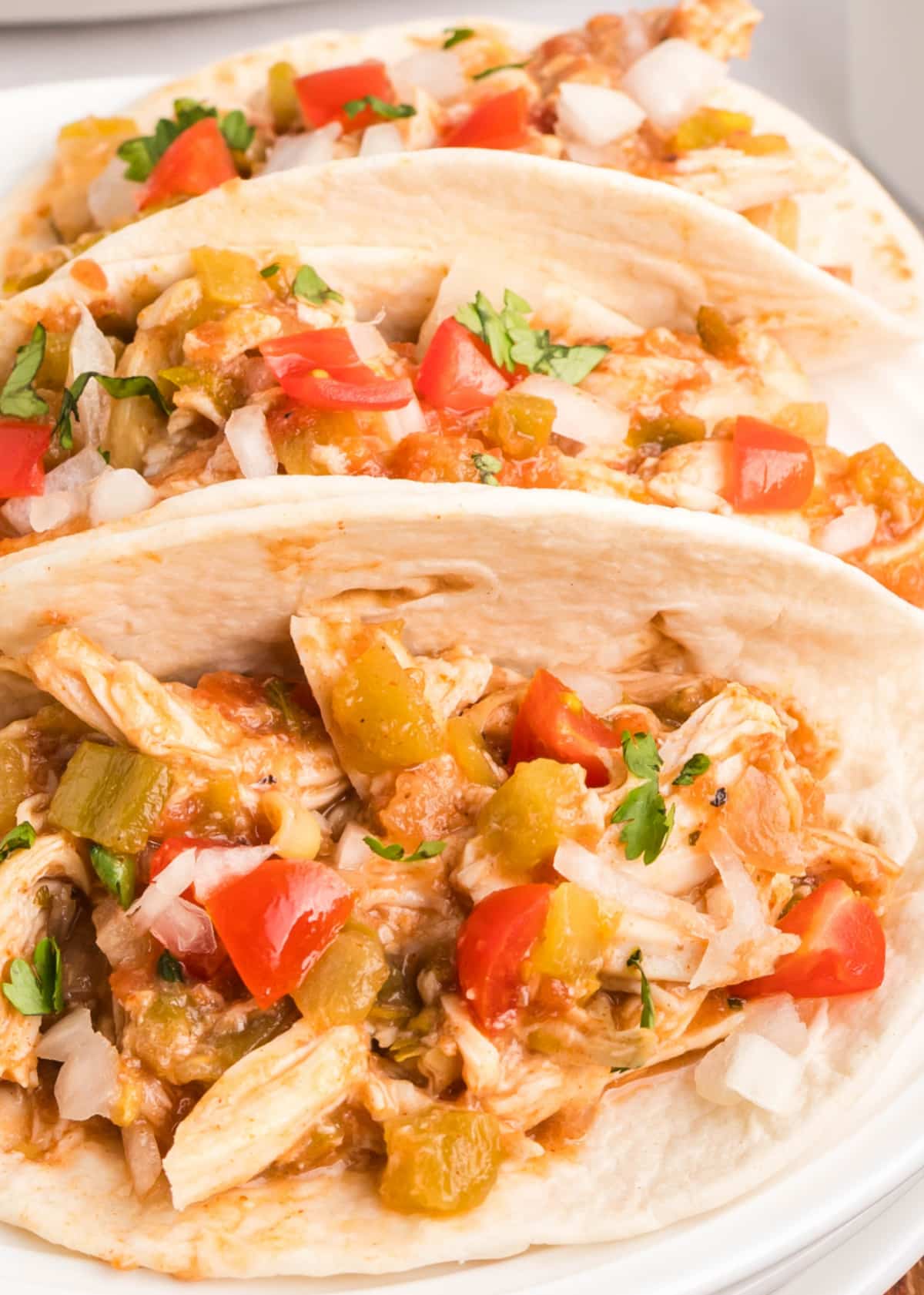 Slow Cooker Shredded Taco Chicken for dinner Overhead view of shredded taco chicken served in soft flour tortillas with toppings.