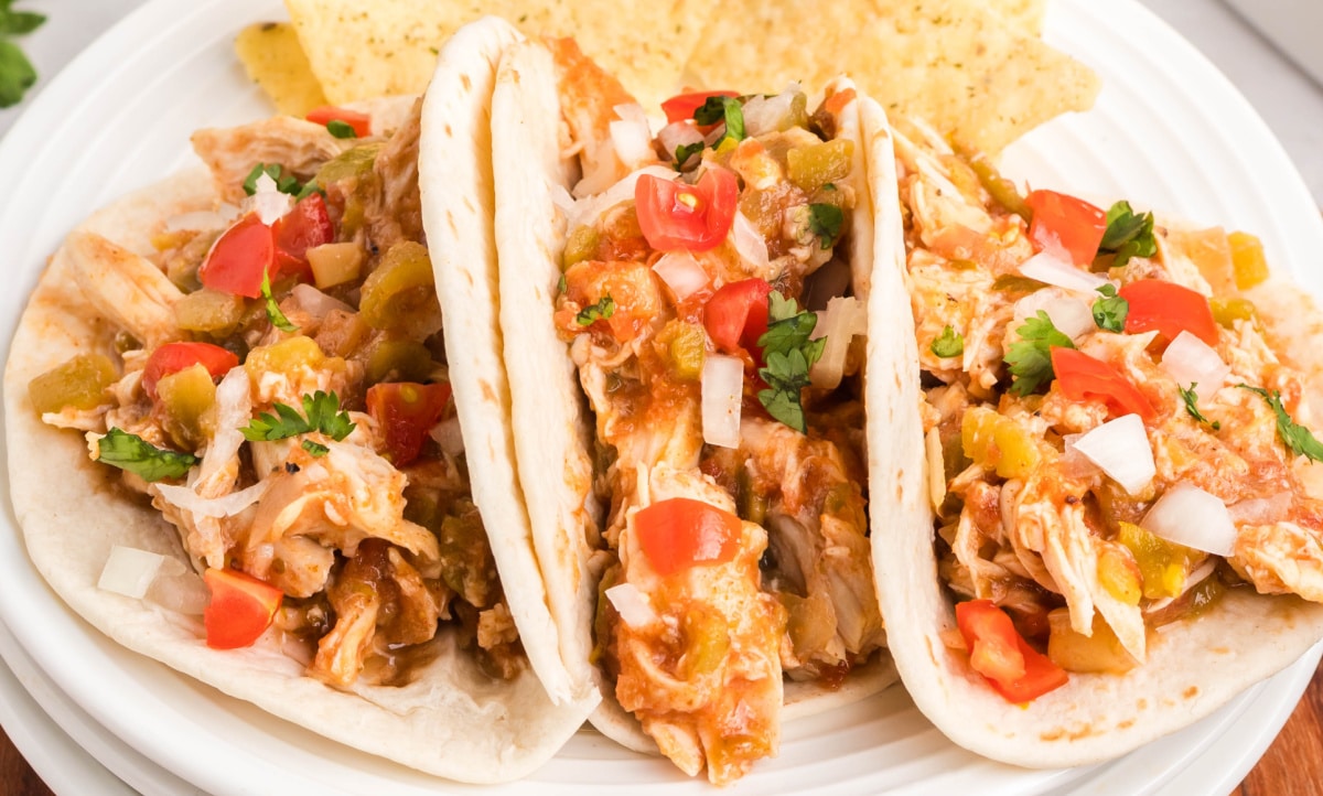 Slow Cooker Shredded Taco Chicken on a plate Close-up shot of slow cooker taco chicken tucked into flour tortillas with fresh garnishes.