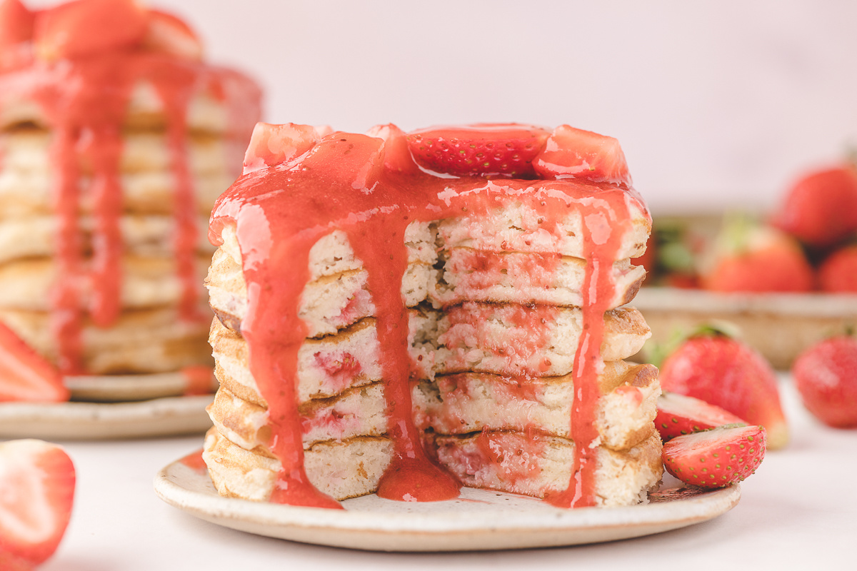 Fresh Strawberry Pancakes with Jammy Berries Fresh strawberry pancakes sliced open to show jammy strawberry pockets inside the buttermilk pancake stack with warm strawberry sauce poured over the top.