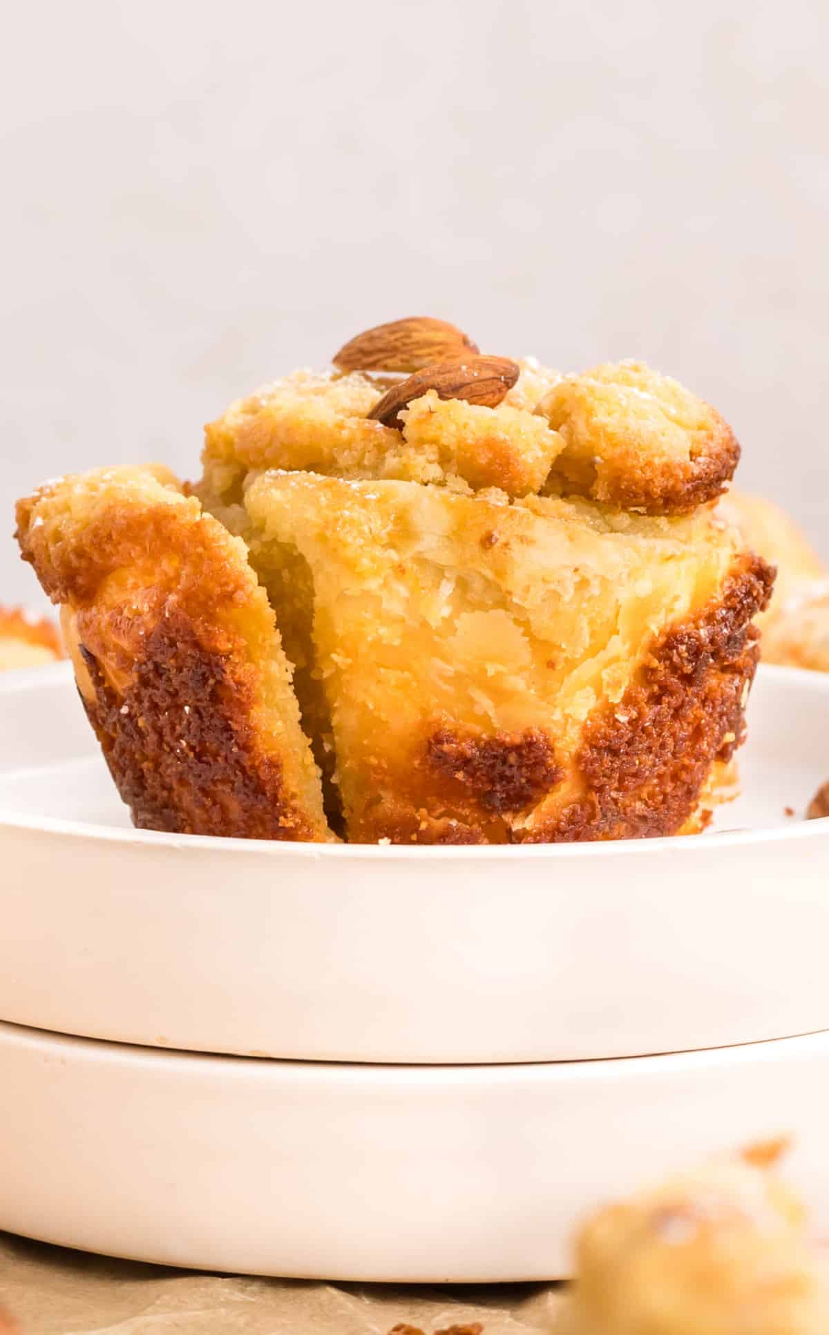almond cruffin on a plate Side view of a single baked cruffin sitting on a small stack of plates, highlighting the flaky layers and browned edges.